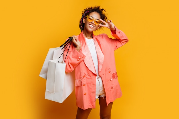 Tiro del estudio de la mujer bastante negra con el bolso de compras blanco que se coloca sobre fondo amarillo. primavera de moda look de moda.