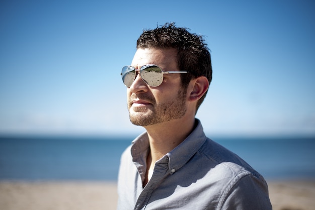 Tiro de foco superficial de un hombre con gafas de sol en la playa en un día soleado