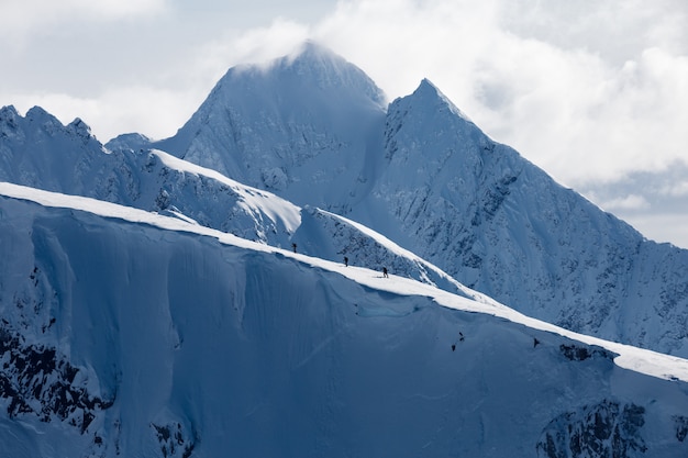 Foto gratuita tiro horizontal de altas montañas cubiertas de nieve bajo nubes blancas y un grupo de personas caminando