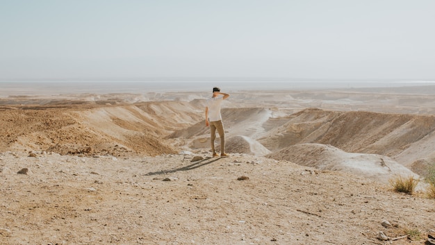 Tiro horizontal de un hombre con una camisa blanca de pie en el borde de una montaña disfrutando de la vista
