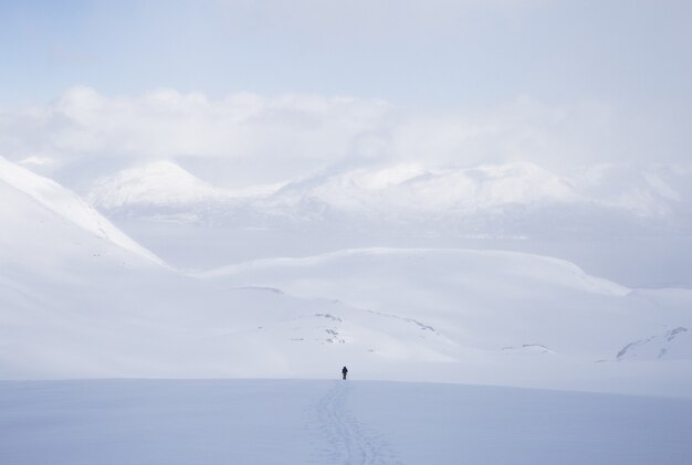 Tiro horizontal de un hombre de pie en una zona nevada con muchas montañas altas cubiertas de nieve