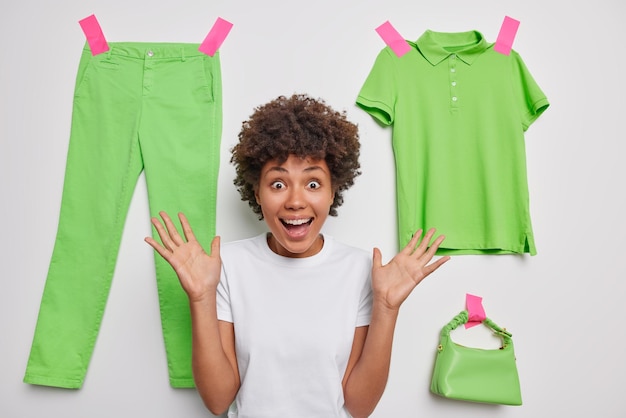 Foto gratuita tiro horizontal de mujer joven feliz emocional exclama en voz alta mantiene las palmas levantadas reacciona en poses increíbles sobre fondo blanco con ropa verde enyesada dice wow, eso es genial