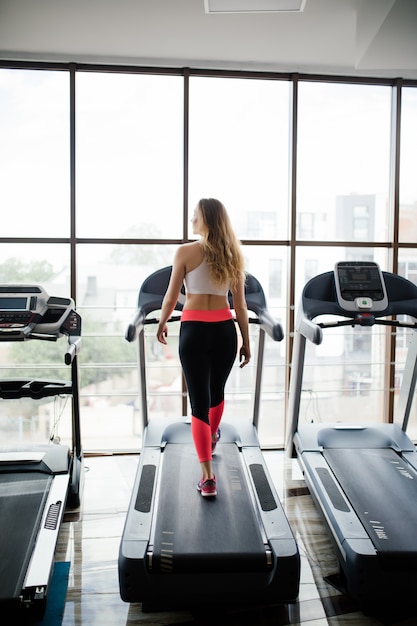 Tiro horizontal de mujer trotar en cinta en el club de salud. Mujer trabajando en un gimnasio corriendo en una cinta.