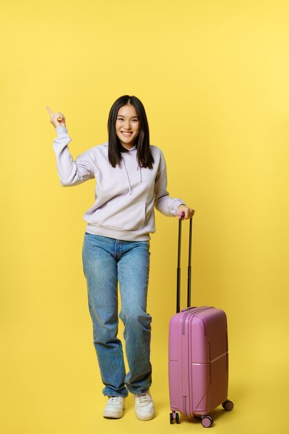 Tiro integral del viajero asiático sonriente de la muchacha del turista que señala en el anuncio del promo que se coloca con ...