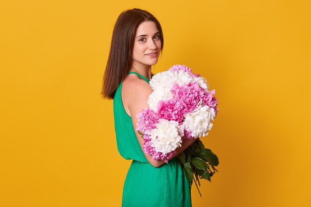 Tiro interior del retrato de una mujer encantadora con estilo en elegante vestido verde aislado sobre amarillo