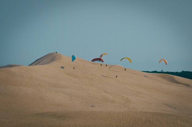 Tiro de largo alcance de parapentes aterrizando en una duna de arena con cielo azul claro