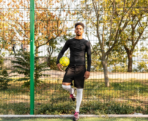 Foto gratuita tiro largo hombre afroamericano posando con una pelota de fútbol