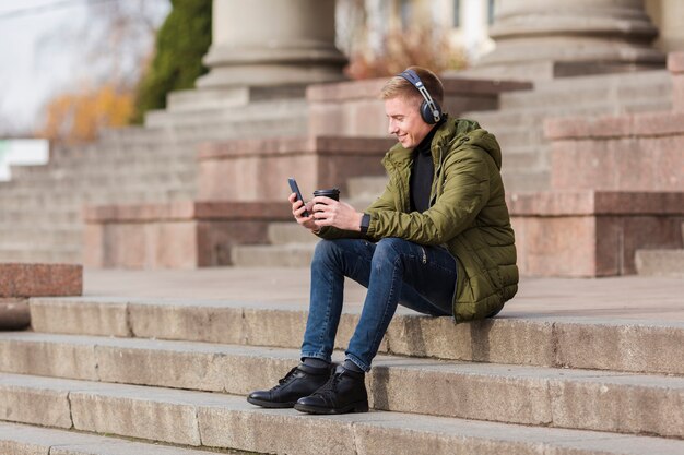 Tiro largo joven escuchando música con auriculares fuera