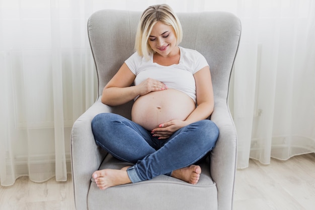 Foto gratuita tiro largo mujer embarazada sentada en el sillón