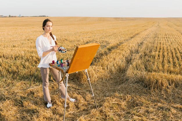 Tiro largo mujer pintura en la naturaleza