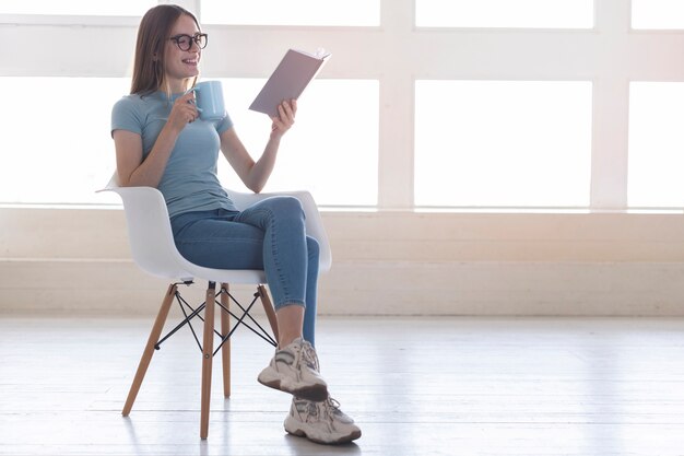 Tiro largo mujer sentada en una silla mientras lee un libro