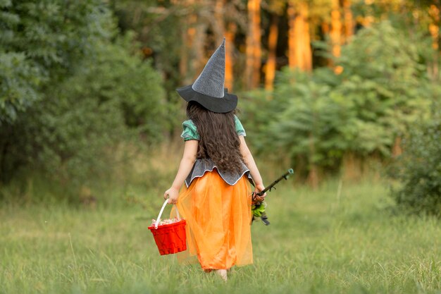 Tiro largo de niña con disfraz de halloween de bruja en la naturaleza