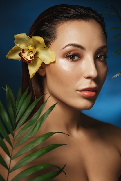 Foto gratuita tiro lateral de la mujer atractiva que se coloca detrás de las flores exóticas.