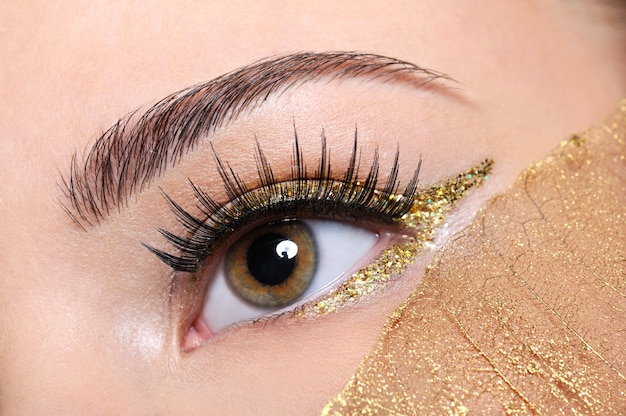 Tiro de macro de un ojo de mujer con pestañas postizas y maquillaje amarillo, dorado