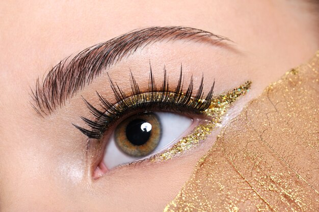 Tiro de macro de un ojo de mujer con pestañas postizas y maquillaje amarillo, dorado