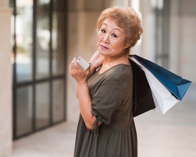 Foto gratuita tiro medio anciana sosteniendo bolsas de la compra.