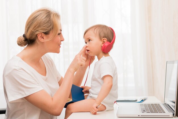 Tiro medio bebé en el escritorio con auriculares y madre sonriendo