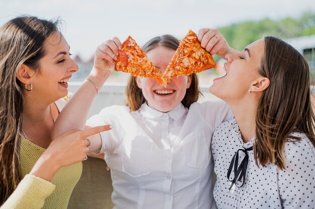 Tiro medio chicas felices con rebanadas de pizza