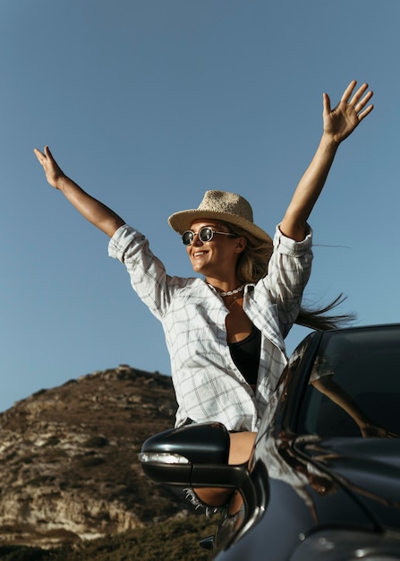 Tiro medio feliz mujer rubia de pie fuera de la ventanilla del coche en la playa