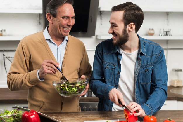 Tiro medio feliz padre e hijo haciendo ensalada en la cocina