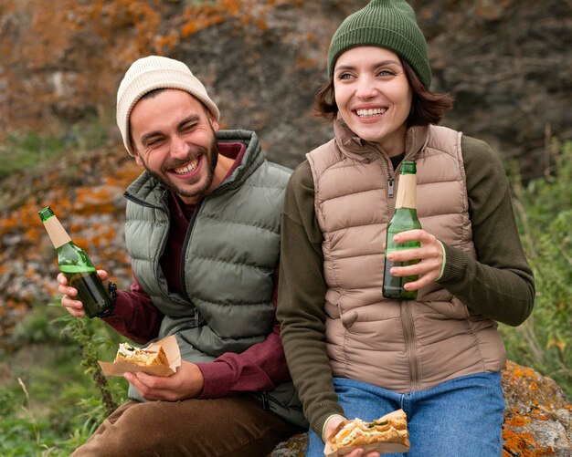 Tiro medio feliz pareja sentada sobre una roca y tomar una copa