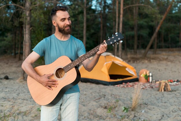 Tiro medio hombre acampando tocando la guitarra