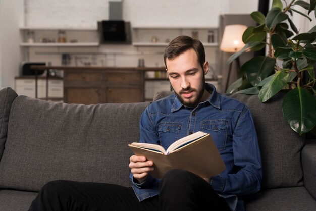 Tiro medio hombre sentado en el sofá y leyendo el libro