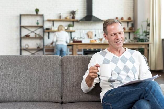 Tiro medio hombre sonriente leyendo en el sofá