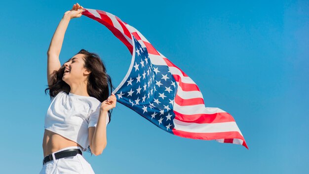 Tiro medio joven mujer morena con gran bandera de Estados Unidos