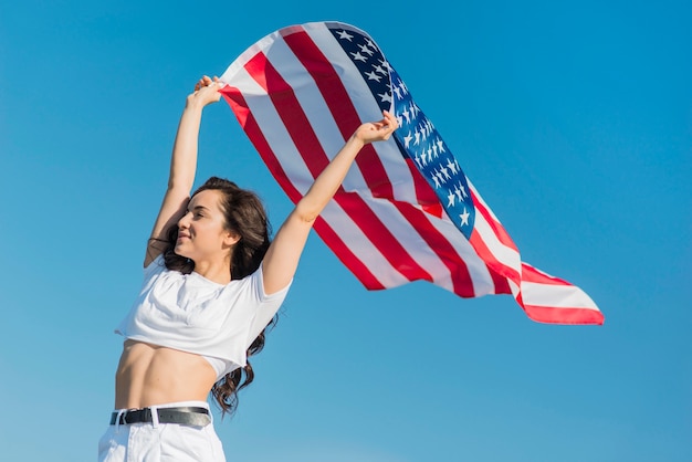 Tiro medio joven sonriente mujer sosteniendo gran bandera de Estados Unidos