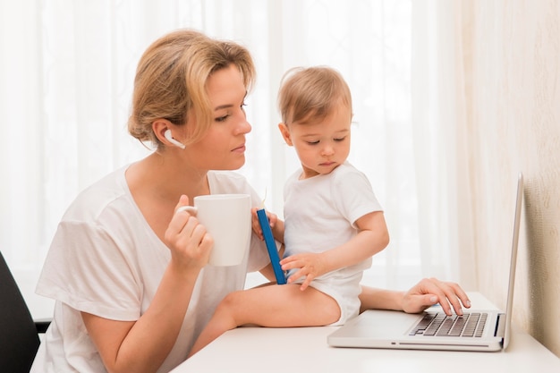 Tiro medio madre bebiendo café y bebé en el escritorio