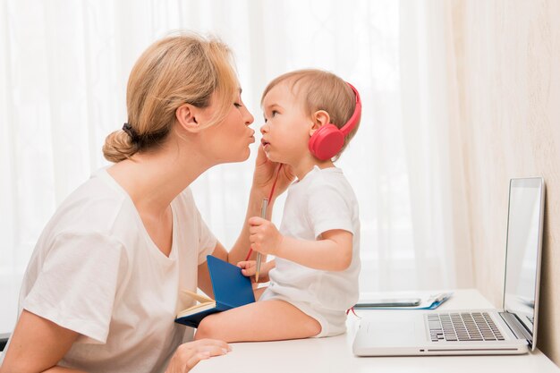 Tiro medio madre besando al bebé en el escritorio con auriculares