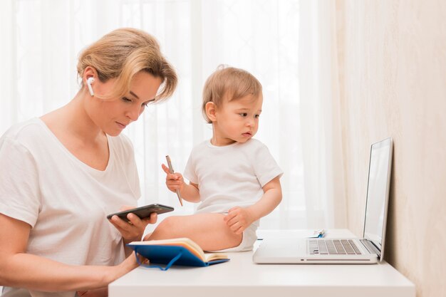 Tiro medio madre mirando el teléfono y el bebé en el escritorio