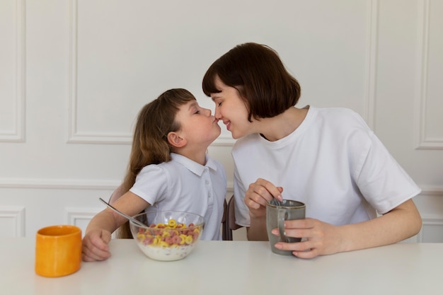 Foto gratuita tiro medio madre y niña sentada en la mesa