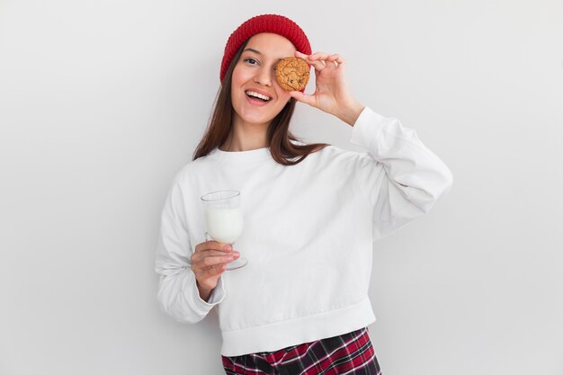 Tiro medio mujer acogedora con sombrero comiendo galletas y leche