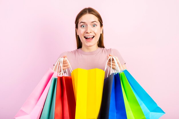 Tiro medio mujer feliz sosteniendo bolsas y mirando a cámara