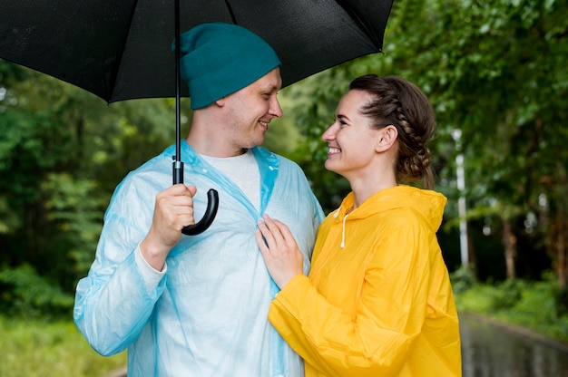 Tiro medio mujer y hombre mirando el uno al otro bajo su paraguas
