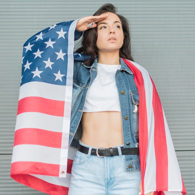 Tiro medio mujer joven con gran bandera de Estados Unidos y saludando a mano