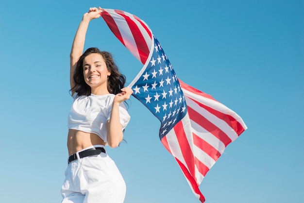 Foto gratuita tiro medio mujer joven con gran bandera de estados unidos y sonriendo