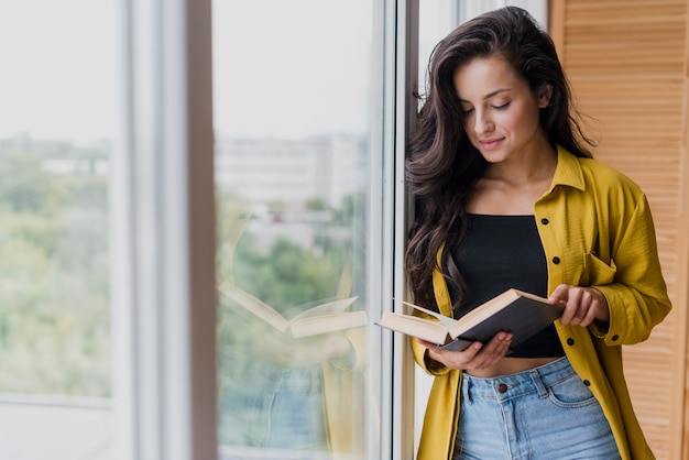 Tiro medio mujer leyendo cerca de la ventana