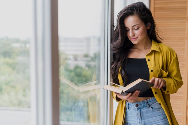 Tiro medio mujer leyendo cerca de la ventana