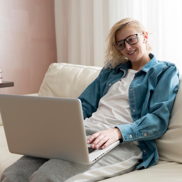 Tiro medio mujer rubia sentada en el sofá y trabajando en la computadora portátil