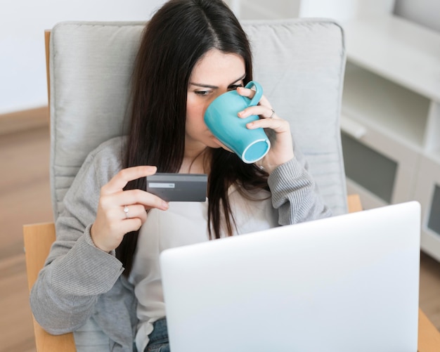 Tiro medio mujer sentada en una silla con laptop y tomando café