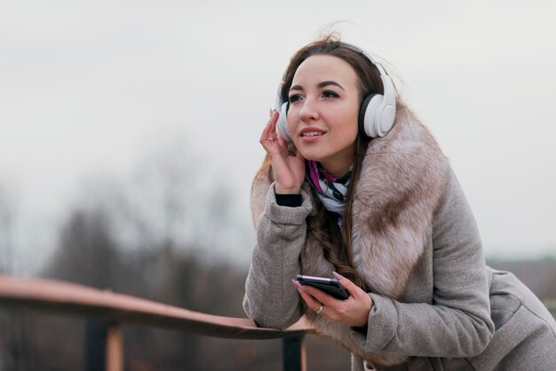 Tiro medio mujer sonriente con auriculares en el techo con teléfono