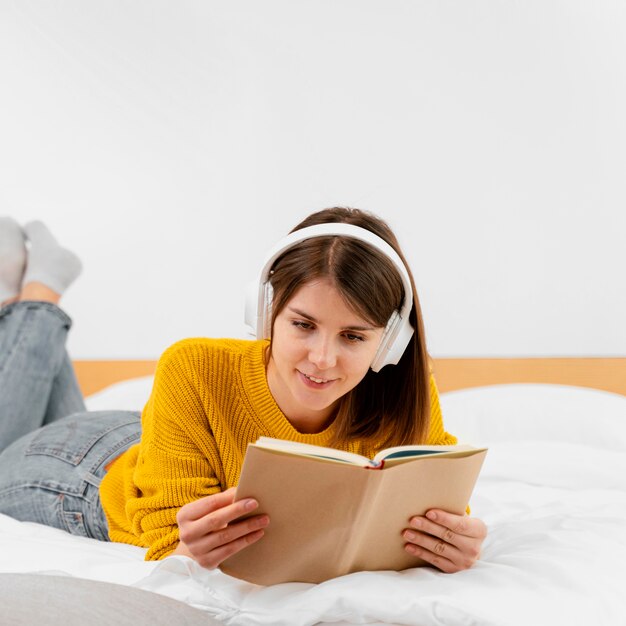 Tiro medio mujer sonriente leyendo en la cama