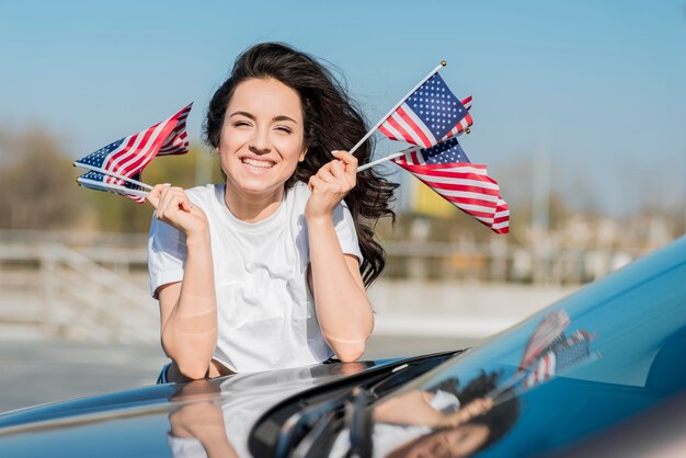 Tiro medio mujer sosteniendo banderas de Estados Unidos en coche