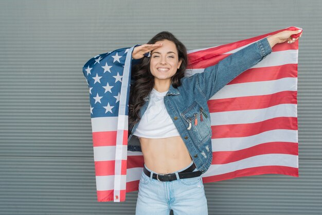 Tiro medio mujer sosteniendo gran bandera de Estados Unidos y saludando a mano