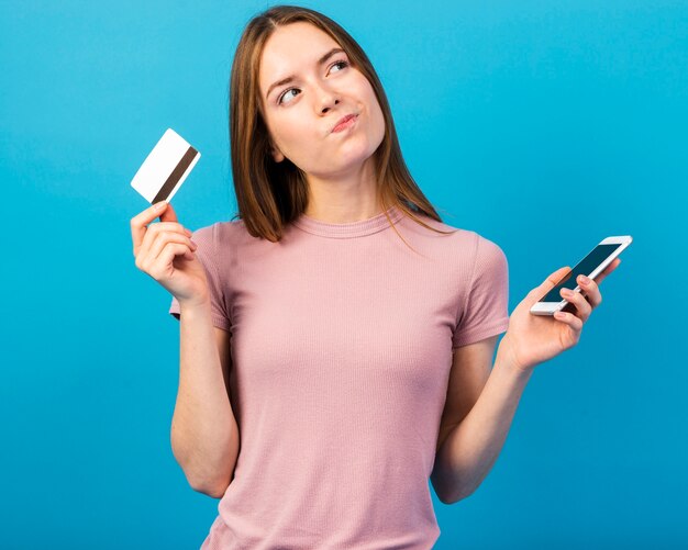 Tiro medio mujer sosteniendo tarjeta de crédito y teléfono y mirando a otro lado