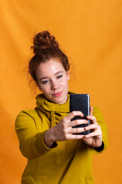 Tiro medio mujer tomando un selfie con fondo naranja