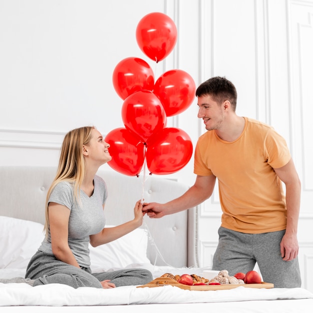 Tiro medio pareja con globos en el dormitorio